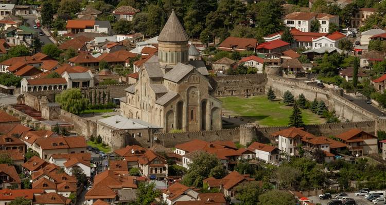 Vista aérea de una iglesia antigua rodeada por una muralla fortificada y techos de tejas rojas.