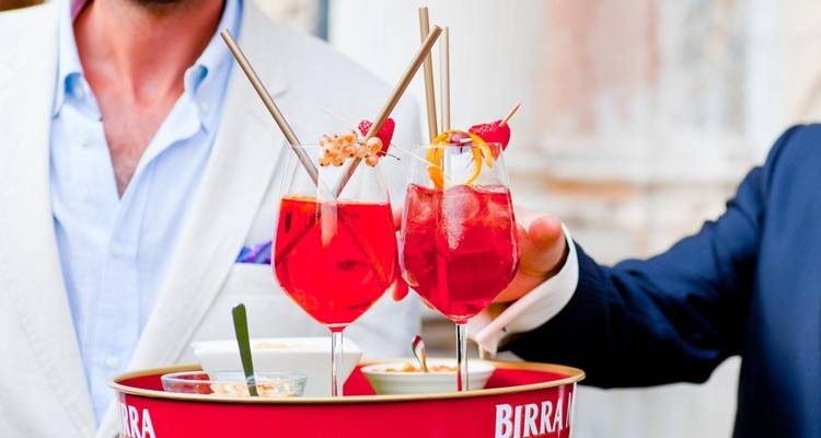 Two people holding a tray with glasses of red cocktails
**Spanish translation:**
Dos personas sosteniendo una bandeja con vasos de cócteles rojos