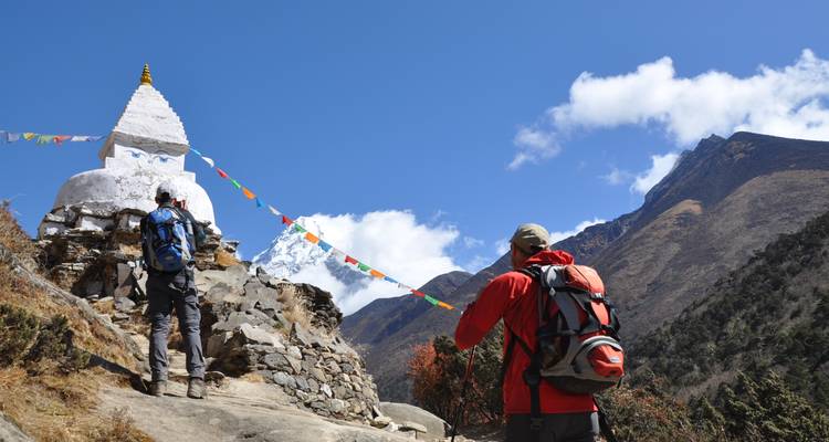 Excursionistas en un sendero con una estupa y banderas de oración en el Himalaya.