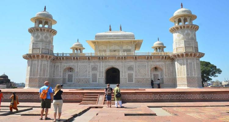 Ein weißes Mausoleum mit kunstvollen Verzierungen und Menschen davor.