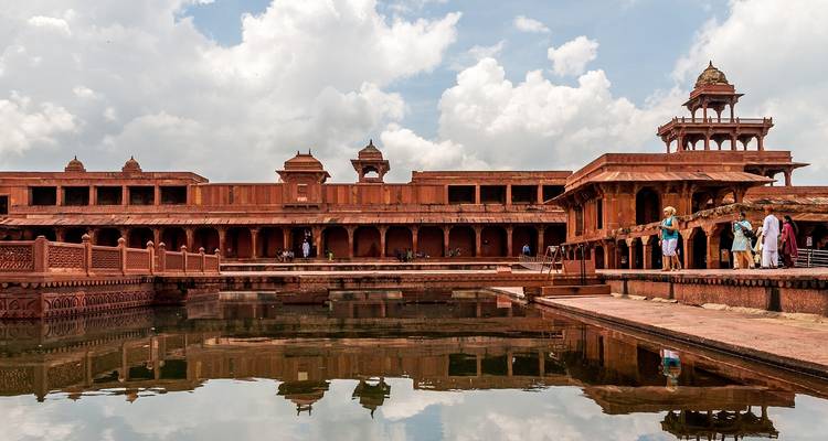 Historische rode zandsteenarchitectuur met een reflecterende vijver en wandelende mensen.