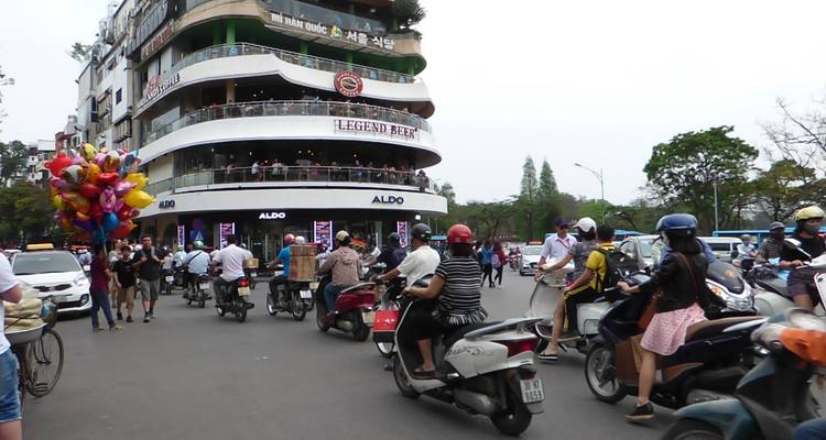 Drukke stadsstraat met voertuigen en mensen, inclusief een verkoper met ballonnen.