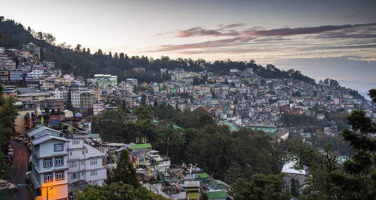 Here's the German translation:
"Hügelige Stadtlandschaft in der Dämmerung mit bunten Gebäuden."