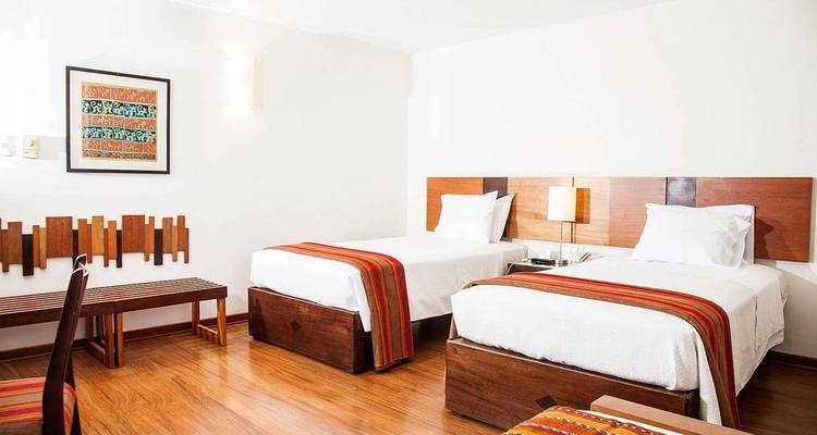 Modern hotel room with two beds and wooden furniture.