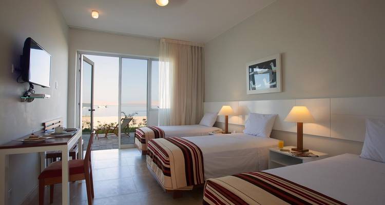 Modernes Hotelzimmer mit drei Betten und Balkonblick.