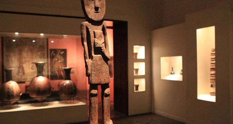 Museumsinterieur mit Kulturgütern und einer Holzstatue.