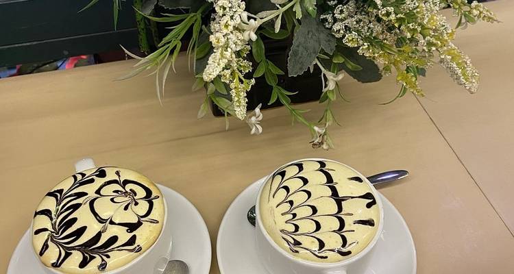 Deux tasses de café décorées à côté de fleurs sur une table.