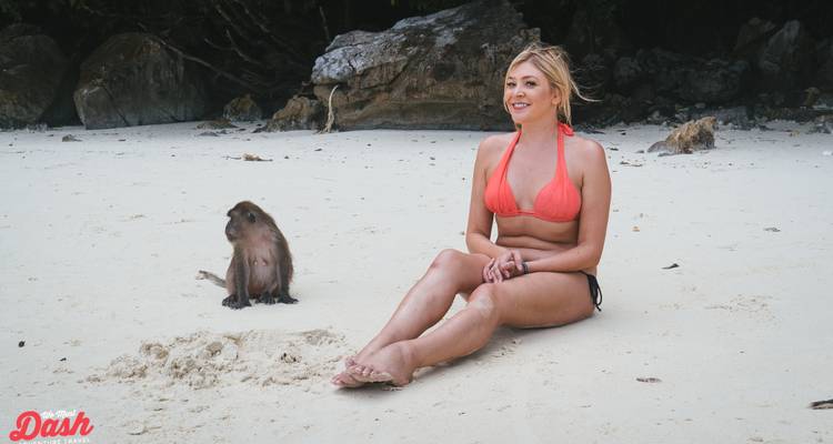 Persona en bikini sentada en una playa con un mono cerca.