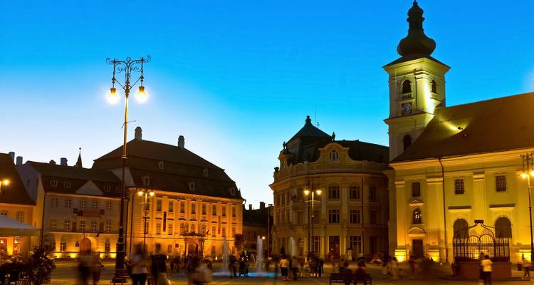 Illumination nocturne de la place principale de Sibiu avec le mouvement flou des visiteurs en promenade.