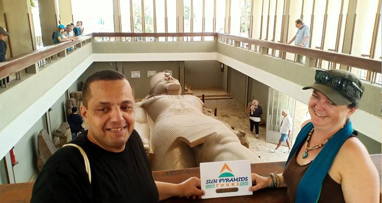 Couple avec un panneau devant une grande statue allongée.