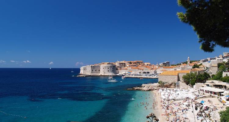 Beachfront with clear blue waters and historic fort-like architecture.