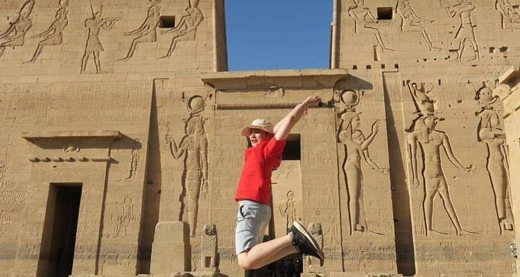 Persoon die springt voor de Philae Tempel met hiërogliefen.