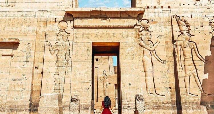 Een persoon in een rode jurk die staat voor een oude Egyptische tempel met grote gegraveerde figuren.