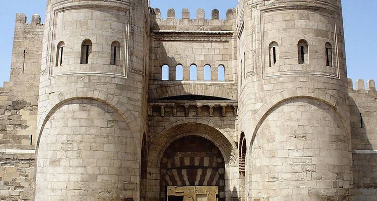 Massieve stenen vestingingang met ronde torens en blauwe lucht.