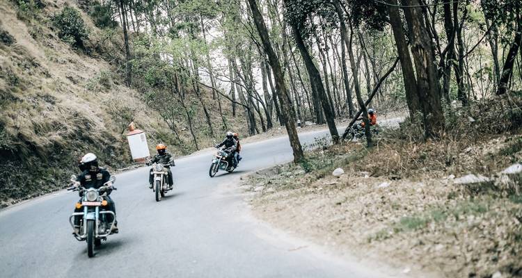 Motorrijders op een bergweg met mensen die brandhout dragen.