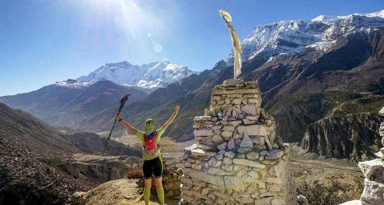 Abenteurer, der triumphierend die Arme in die Höhe streckt, neben einem Steinmännchen vor einer Berglandschaft.