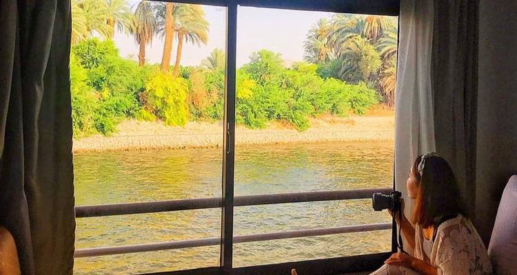 Woman inside looking out at lush greenery through a large window.