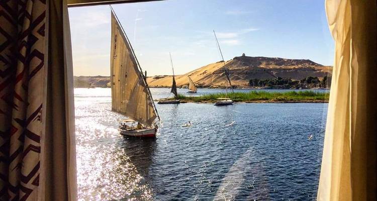 Sailboats on a river seen through a window with sunlight reflecting.