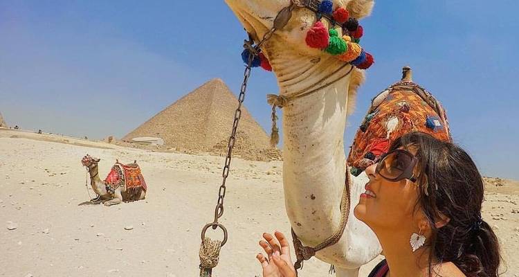Eine Frau mit einem Kamel vor den Pyramiden.