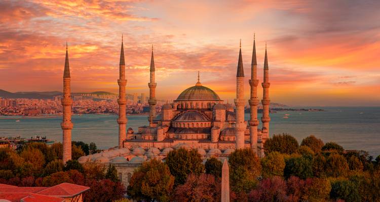 La majestuosa Mezquita Azul y sus minaretes iluminados por la cálida luz del atardecer con vista al Bósforo.