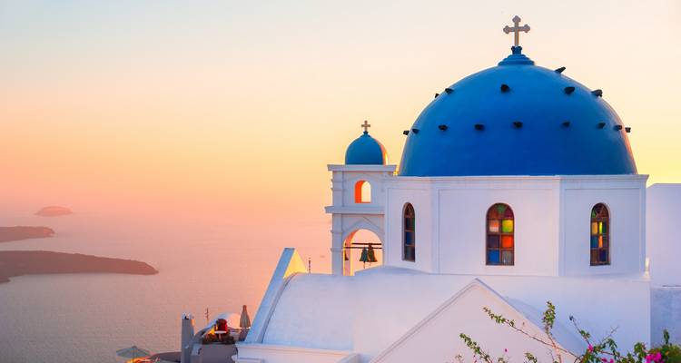 Ikonische blaudomige Kirche mit Blick auf die Caldera bei Sonnenuntergang in Santorin.