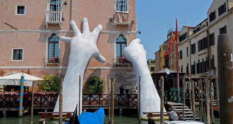 De grandes mains blanches sculptées émergent du Grand Canal, soutenant un palazzo vénitien.