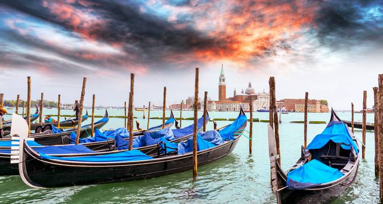 Rangée de gondoles couvertes de bleu amarrées avec des nuages dramatiques et enflammés au-dessus de San Giorgio Maggiore.