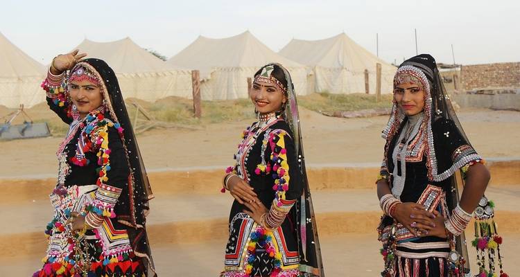 Trois femmes en robes traditionnelles colorées exécutant une danse dans un décor désertique.