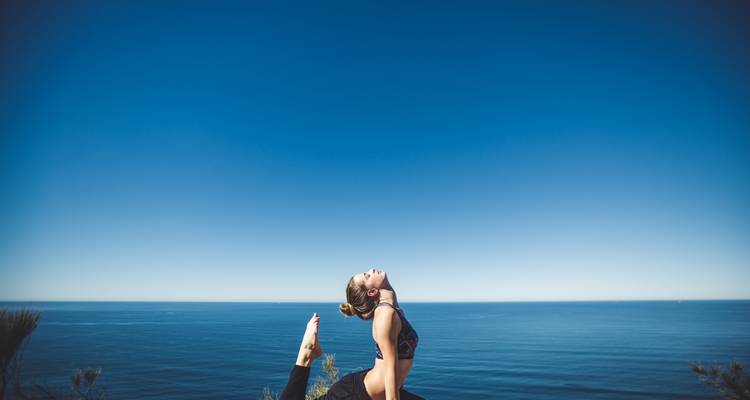 Solo yogi performing a backbend pose on coastal cliff with expansive blue sea