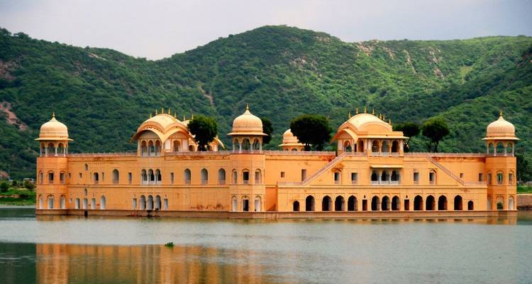Palais aquatique Jal Mahal aux tons ambrés flottant sur un lac calme avec des collines vertes en arrière-plan
