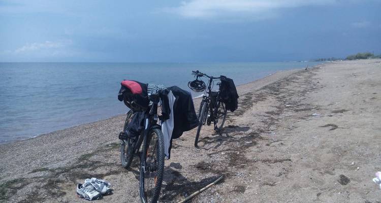 Zwei Fahrräder, die an einem sandigen Strand geparkt sind, mit ruhiger See im Hintergrund.