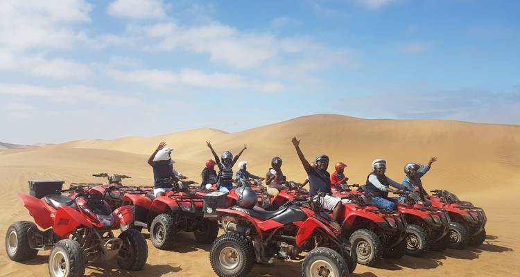 Group of people on quad bikes in a desert setting.