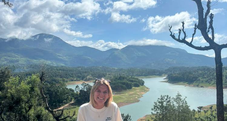 Voyageur souriant posant devant un lac serein entouré de montagnes luxuriantes au Kerala