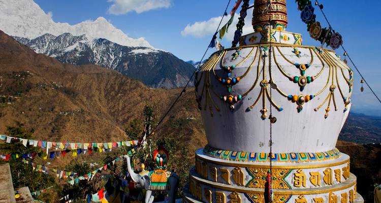 Stupa with colorful flags and mountains in the background.