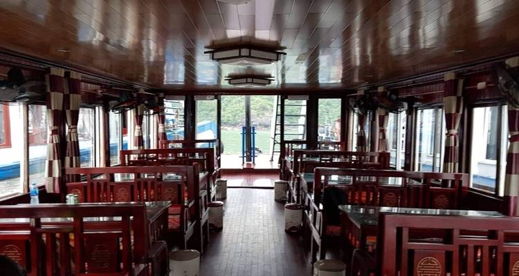 Interior of a boat with dining tables and chairs, view of water through large windows.