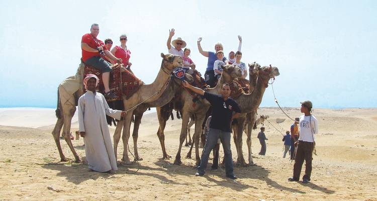 Große Gruppe von Menschen auf Kamelen in der Wüste, die für ein Foto posieren.