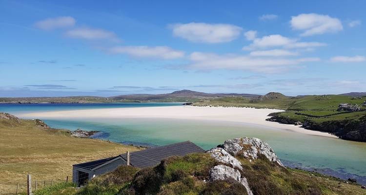 Playa con agua azul cristalina y un pequeño edificio en la orilla.