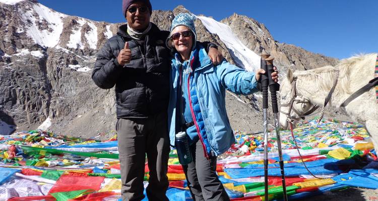 Two people in winter clothing with prayer flags on a mountainous landscape.