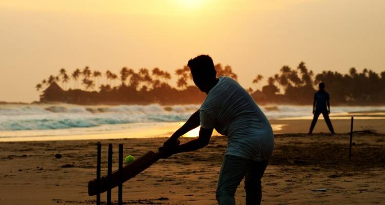Silueta de personas jugando cricket en la playa al atardecer.