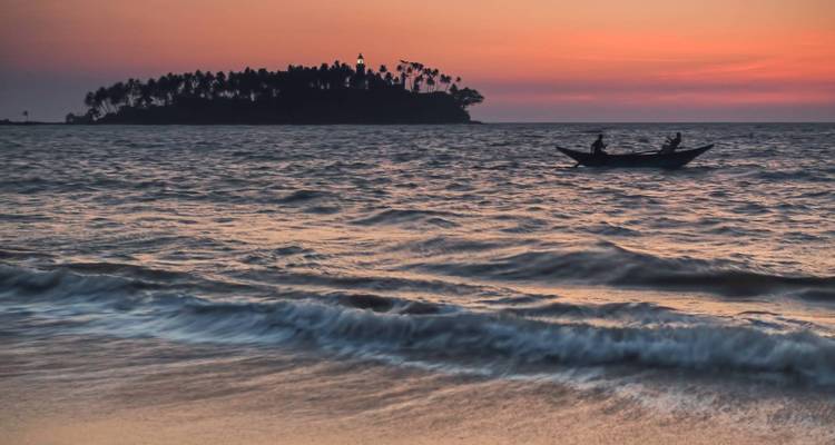Friedlicher Meerblick bei Sonnenuntergang mit Silhouetten von Bäumen und einer Insel.