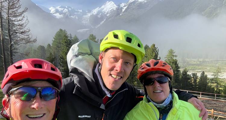 Tres ciclistas posando con montañas nevadas de fondo.