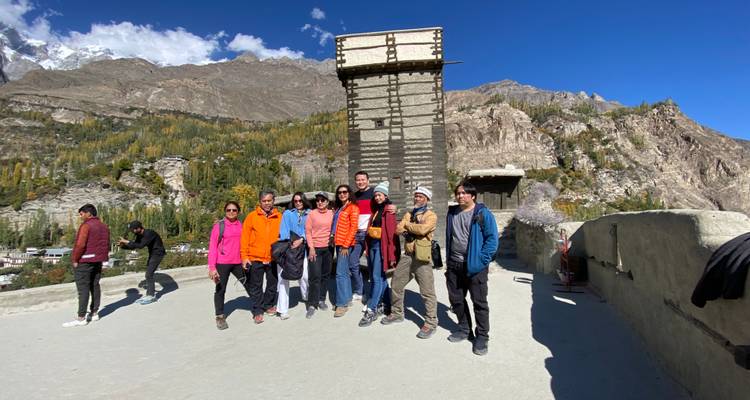 Grupo de turistas posando con un fuerte histórico y montañas de fondo.