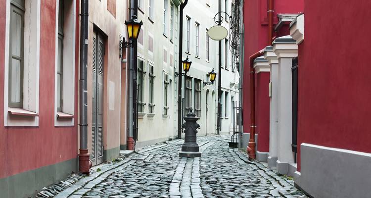 A narrow cobblestone street lined with colorful buildings and street lamps.