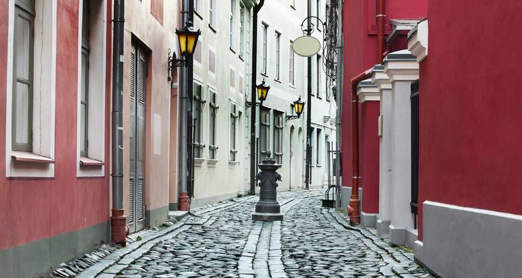 Calle de adoquines estrecha con fachadas coloridas y lámparas vintage en el casco antiguo de Riga.