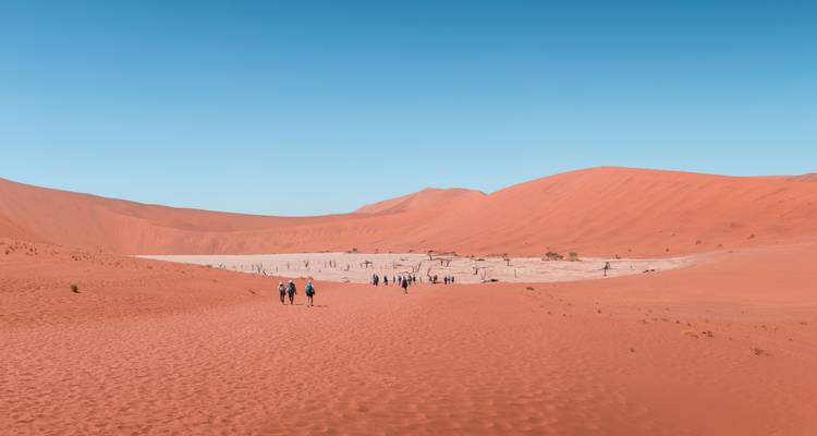 Kleine groep die over een kaal rood woestijnlandschap loopt.