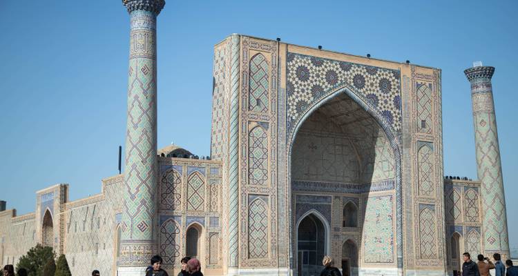 Verzierter Madrasa-Eingang mit hoch aufragendem Minarett und Besuchern an der Basis