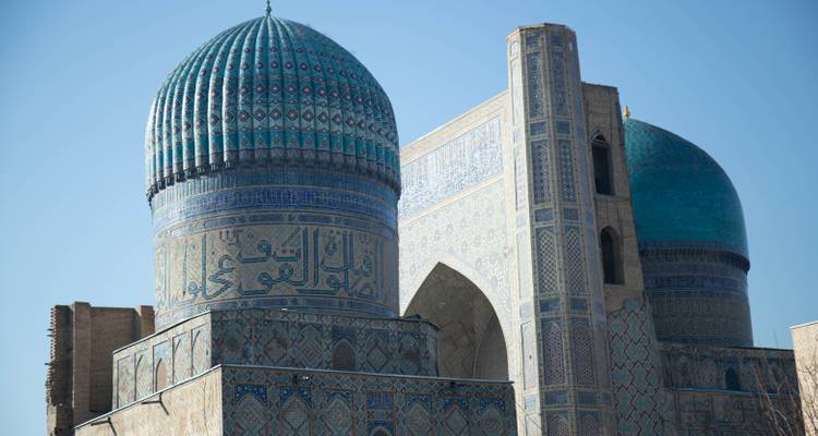 Nahaufnahme einer strahlenden türkisfarbenen Mosaikkuppel und gewölbten Fassade vor blauem Himmel