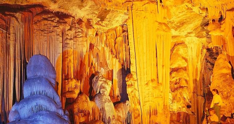 Estalactitas y estalagmitas dentro de una cueva, iluminadas cálidamente.