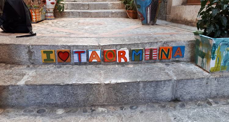 Buntes Straßenschild mit der Aufschrift 'I ♥ TAORMINA' auf Steinstufen.
