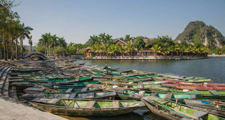 Een uitzicht op talrijke kleine bootjes aangemeerd aan een rivier met bomen en verre bergen.